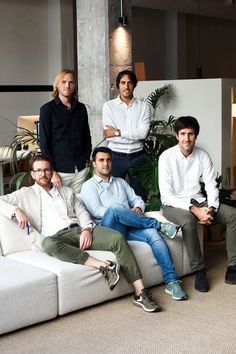 the men are sitting on the couch posing for a group photo in front of some plants