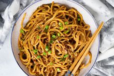 a bowl filled with noodles and chopsticks on top of a white table cloth