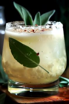 a close up of a drink in a glass with a green leaf on the rim