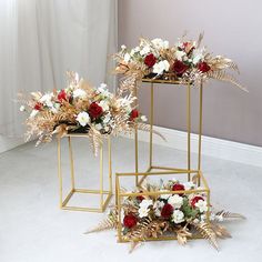 two gold plant stands with flowers in them on the floor next to a white wall