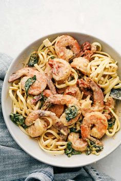 pasta with shrimp and spinach in a white bowl on top of a blue towel