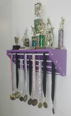 a purple shelf with medals and other trophies hanging on it's sides in front of a white wall