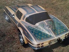 an old model car painted with blue and yellow designs on it's side, sitting in the grass