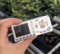 a person holding up a cell phone in front of some trees and bushes with their hands