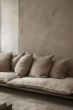 a couch with many pillows on it in front of a window and rugs by the wall