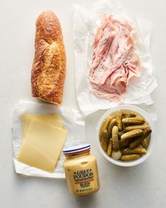 some food is laying out on a white counter top, including bread, cheese and pickles