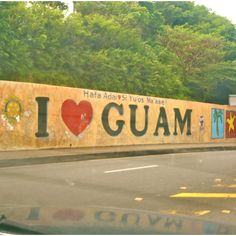 i love guam written on the side of a wall with trees in the background