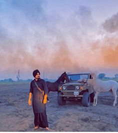 a woman standing in front of a truck with a horse next to it on a dirt field