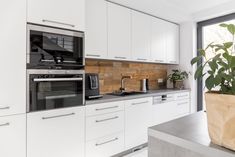 a kitchen with white cabinets and an oven in the center, potted plant next to it