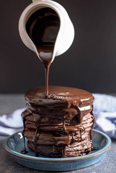 a stack of pancakes covered in chocolate frosting being drizzled with syrup