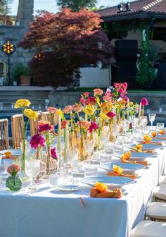 a long table is set with flowers in vases and place settings for the guests