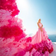 a woman in a pink and red dress standing on top of a snow covered hill