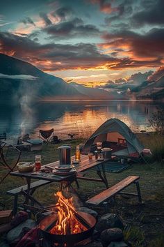 a campfire and picnic table in front of a lake at sunset