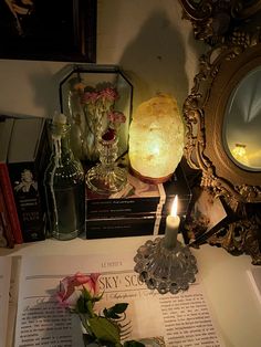 a candle is lit on top of an open book next to some flowers and bottles