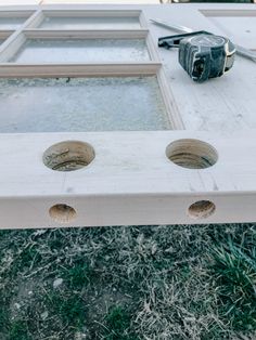 an old window frame with three holes in it and a camera on the ground next to it