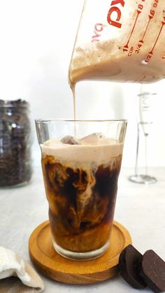 ice coffee being poured into a glass on top of a wooden coaster next to cookies