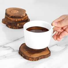 a person holding a cup of coffee in front of some coasters on a marble table