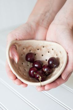 a person holding a bowl with cherries in it