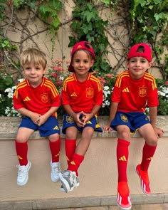 three young boys sitting on a ledge wearing red and yellow soccer uniforms with matching socks