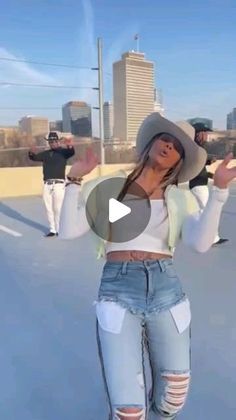 a woman wearing ripped jeans and a cowboy hat is dancing in the middle of an empty parking lot