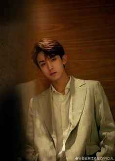 a young man in a white suit standing next to a wooden wall