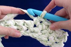 two hands are crocheting together to make a blanket with white and green yarn