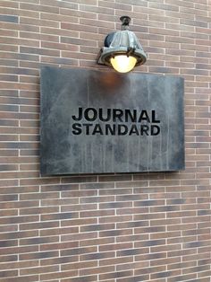 a sign on the side of a brick building that says journal standard with a lamp above it