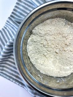 a metal bowl filled with white flour on top of a blue and white striped towel