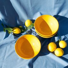 three yellow bowls sitting on top of a blue table cloth with lemons in them