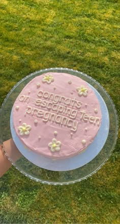 a pink frosted birthday cake sitting on top of a glass plate in the grass