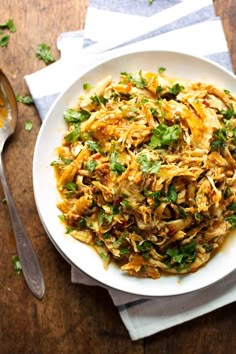 a white bowl filled with food on top of a wooden table next to silverware