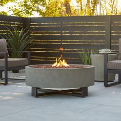 an outdoor fire pit sitting on top of a cement slab next to two chairs and a table