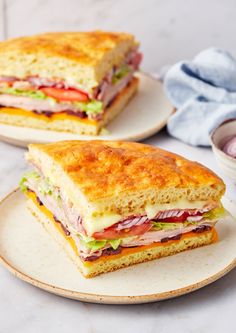 two plates with sandwiches cut in half on top of a white marble countertop next to an empty bowl