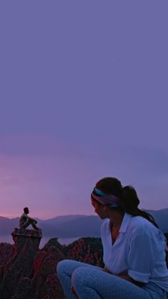 a woman sitting on top of a mountain next to a bird