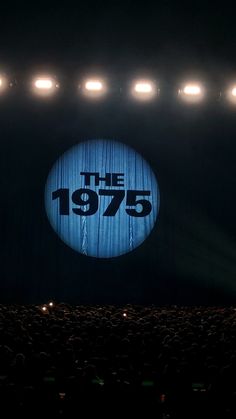 A curtain at a concert has the band logo "The 1975" projected onto it. The 1975 Background, 1975 Concert Aesthetic, The 1975 Wallpaper Iphone, The 1975 Wallpaper Aesthetic, The1975 Aesthetic, The 1975 Lockscreen, Avicii Tattoo