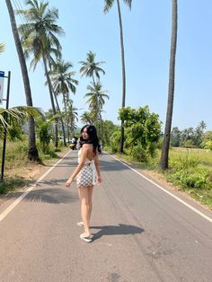 a woman walking down the middle of a road with palm trees in the back ground