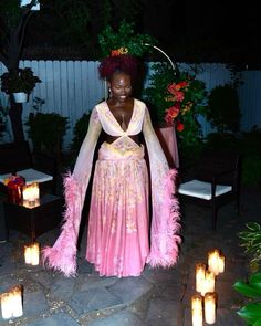 a woman in a pink dress standing next to some lit candles and wearing a feathered shawl