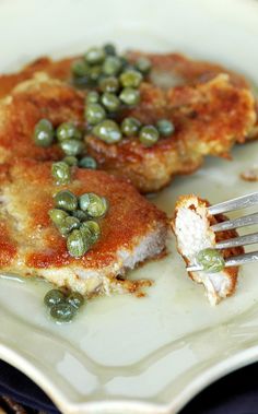 a white plate topped with meat covered in sauce and green peas next to a fork