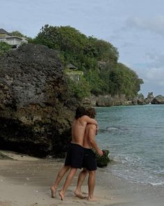 two young men playing frisbee on the beach next to some rocks and water