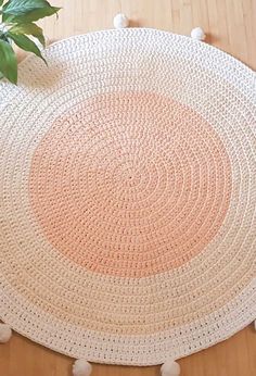 a round rug with pom poms on the floor next to a potted plant