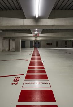 an empty parking garage with red and white markings on the floor, along with lights overhead