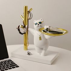 a white bear holding a gold tray with sunglasses on it's head and standing next to a laptop