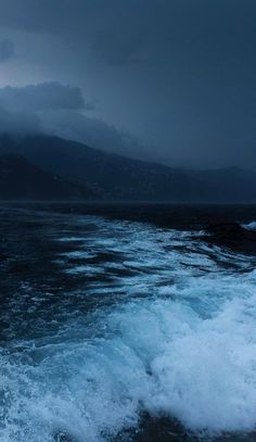 the water is choppy and blue as it moves through the dark ocean with mountains in the distance