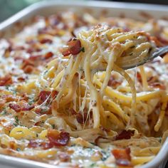 a spoon full of pasta with bacon and cheese on it is being lifted from a casserole dish