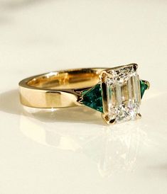 an emerald and diamond ring on a white surface