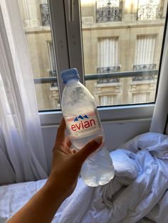 someone is holding a bottle of water in front of a window that looks out onto the street