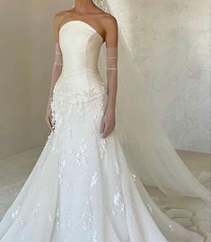 a woman in a white wedding dress standing next to a veil on her head and looking off into the distance