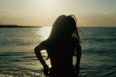 a woman standing in the water at sunset with her back to the camera, looking out into the ocean