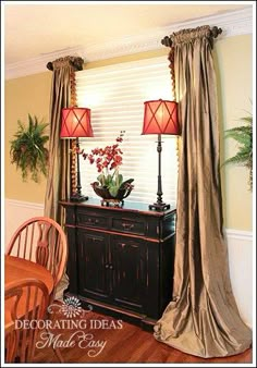 a dining room table with two lamps on top of it next to a window covered in drapes