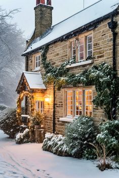 a house covered in snow with christmas lights on the front door and windows, surrounded by evergreens